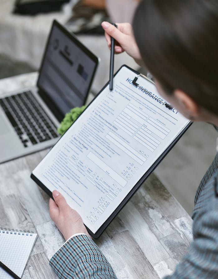 gallery-05 An adult reviews a home insurance policy document at a desk with a pen and laptop.