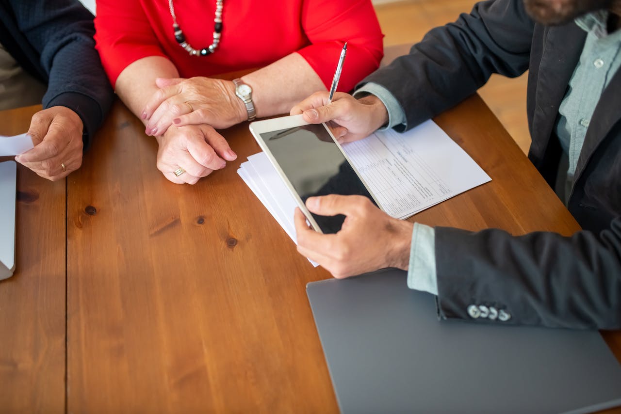 gallery-04 Business meeting at a wooden table with consultant reviewing documents and using a digital tablet.